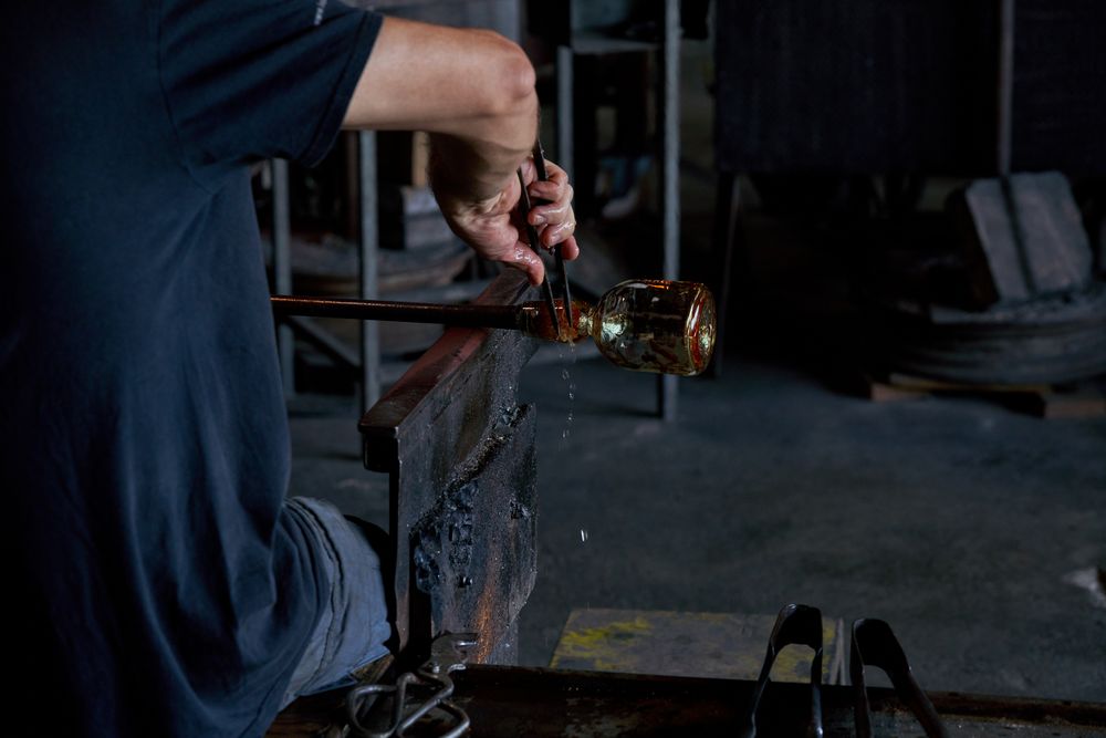 Crop man making glass using rod and tongs in workshop
