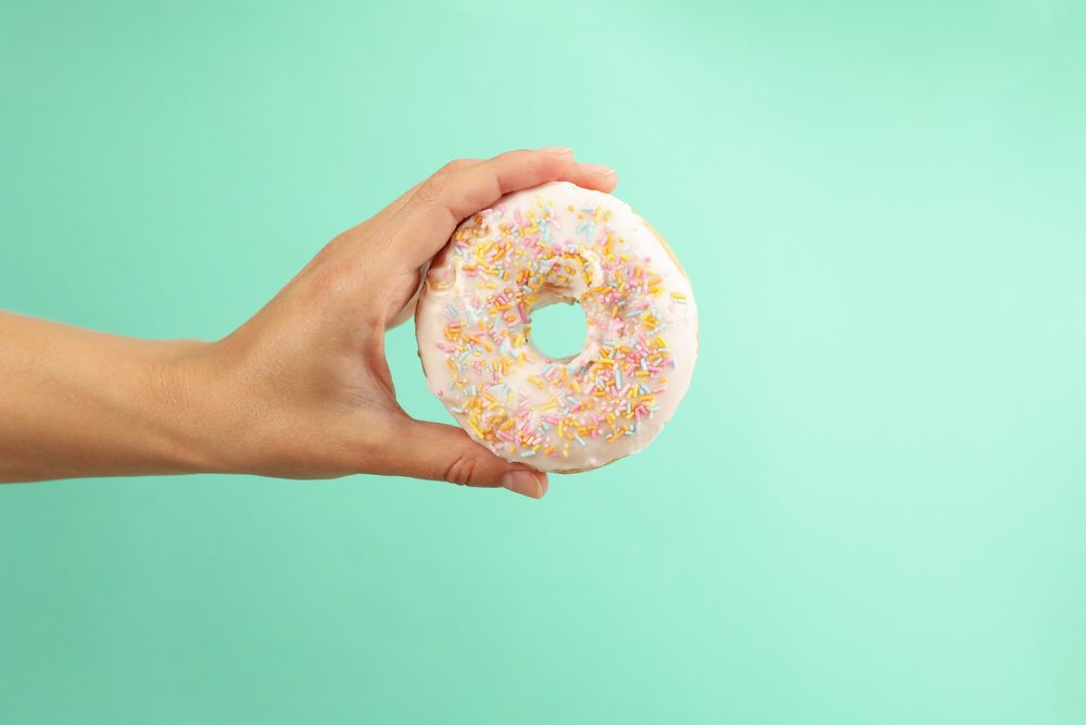 Female hand hold tasty donut on mint background