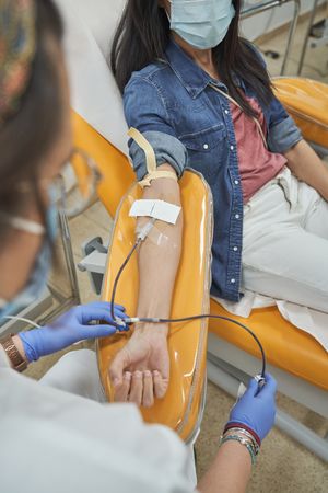 Female patient in mask donating blood in modern clinic