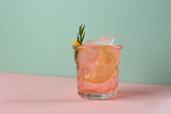 Iced pink drink with rosemary garnish on duo tone background