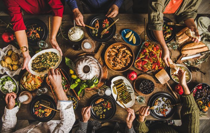 Group of people at wooden table with meze feast and cake