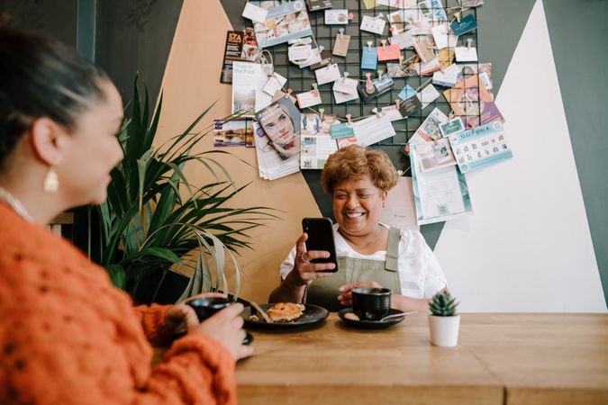 Older Black woman with smart phone at cafe sitting across from daughter