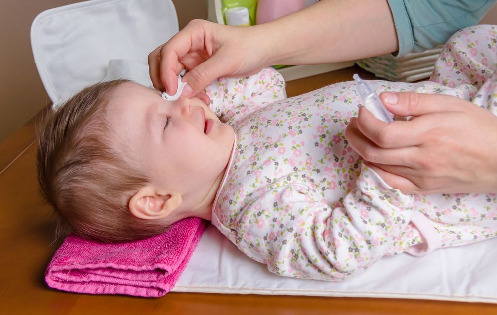 Side view of mother cleaning baby's eyes with cotton