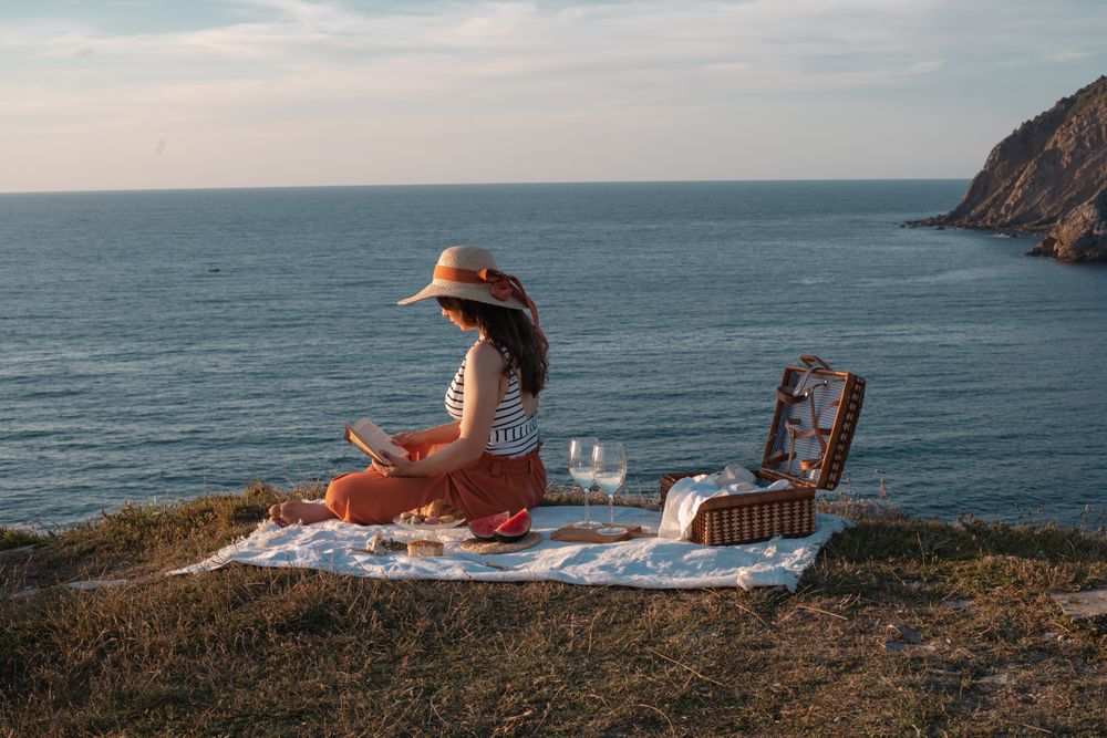 Woman reading on mat for picnic on seashore