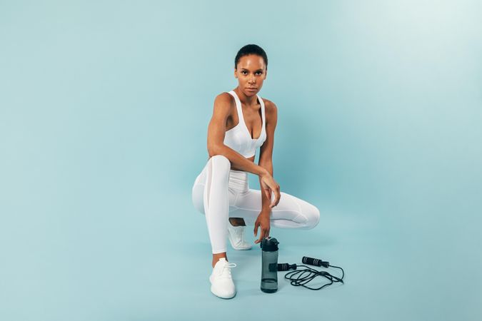 Serious woman sitting in blue studio after working out with jump rope and water bottle