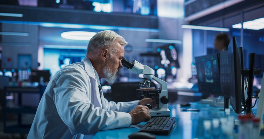 Medical Development Laboratory: Male Scientist Using Microscope, Analyzes Petri Dish Sample.