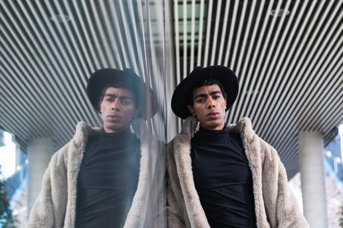 Stylish hispanic man reflecting in glass wall on street