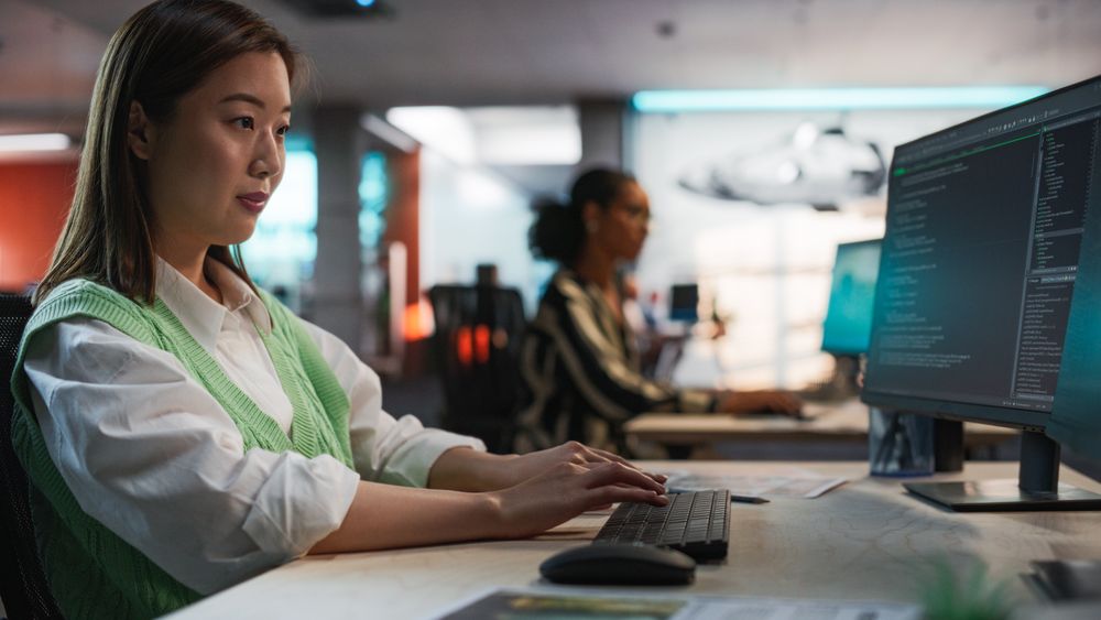 Female Asian Game Programmer Coding On Desktop Computer In Game Development Studio Diverse Office.