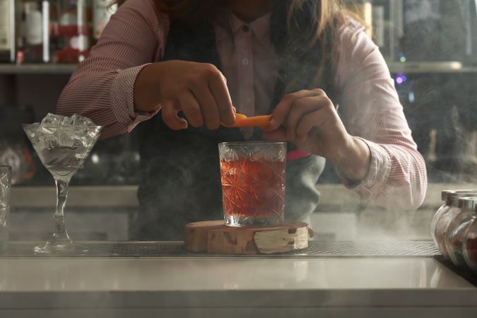 Bartender squeezing orange peel over a Negroni cocktail at the bar