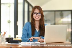 Asian woman wearing glasses and laptop on desk, looking at camera 0We814