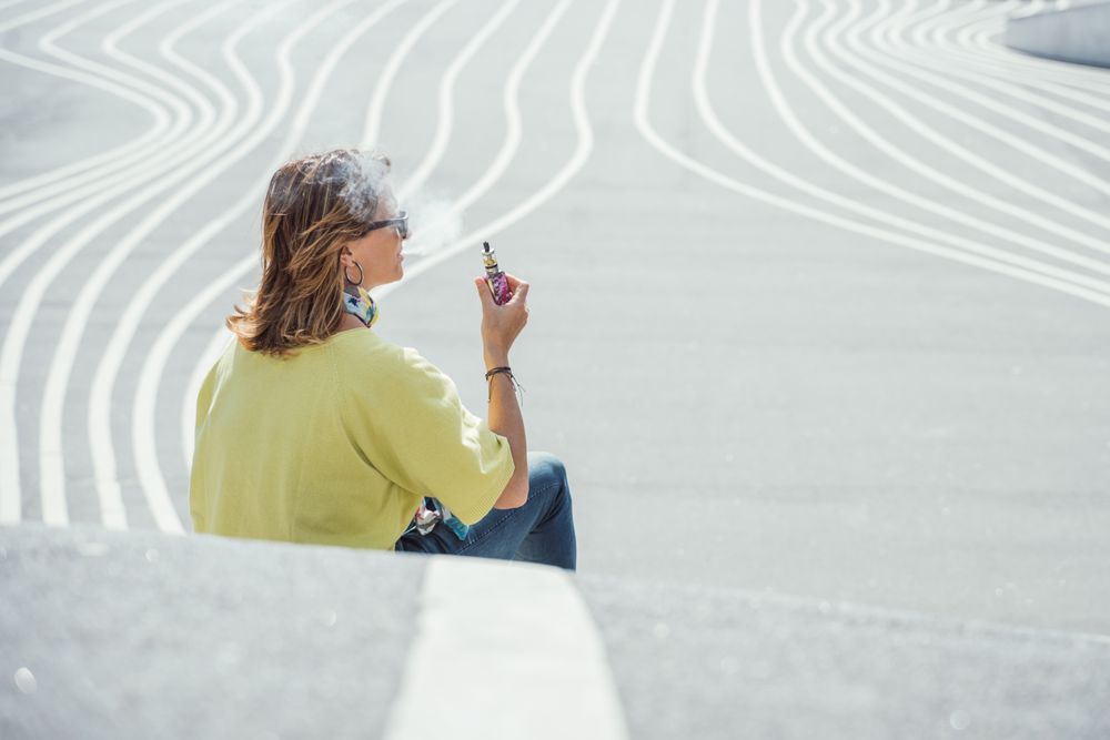 Modern relaxed woman vaping while sitting on marked road
