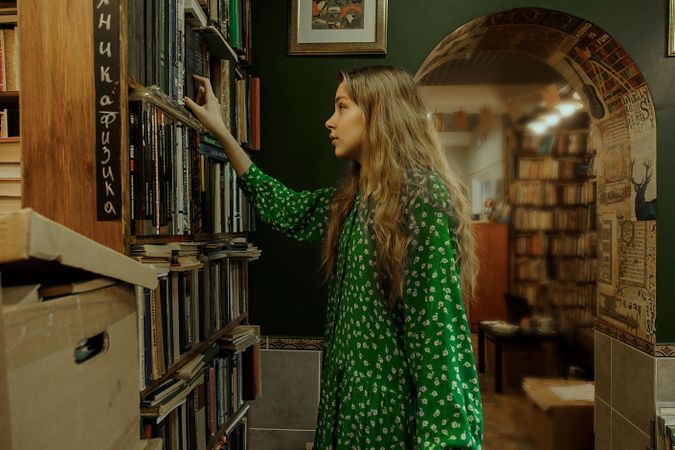 Girl in green polka dot dress taking a book from bookshelves