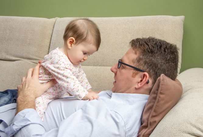 Cute baby playing on father's chest on sofa