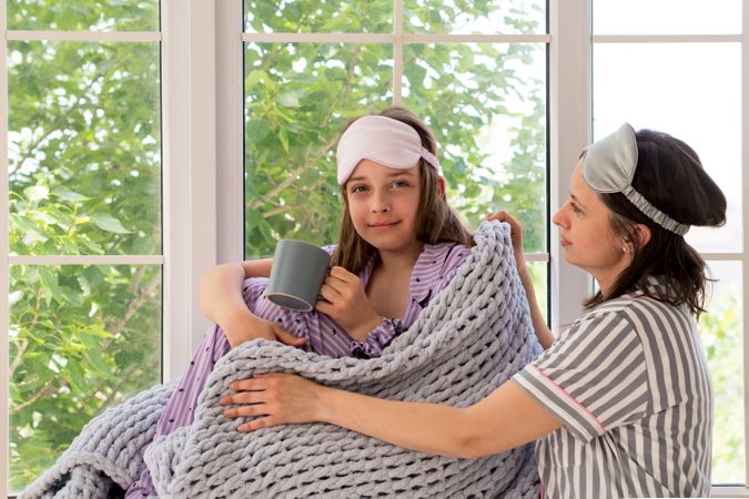 Mother comforting daughter with tea by sunny window.