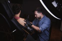 Master doing tattoo on forearm of male customer