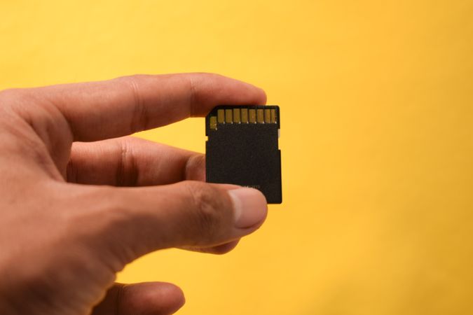Hand holding SD card with yellow background