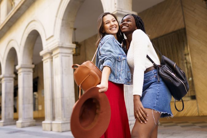 Female friends smiling and standing cheek to cheek on an outdoor street