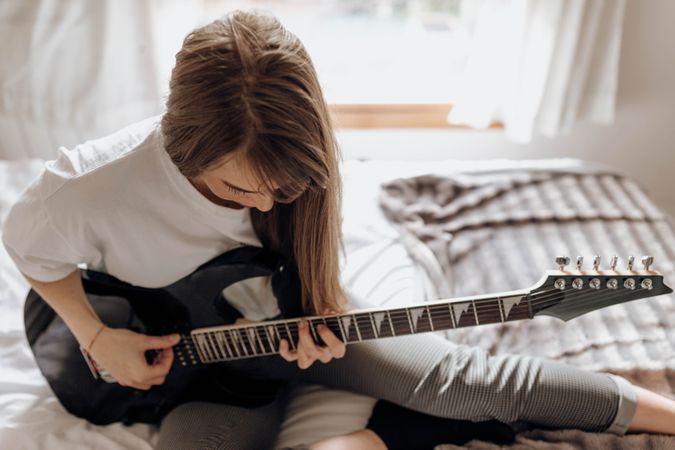 side view of Young brunette woman playing guitar on bed