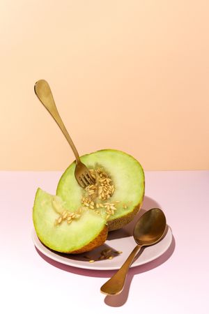 Sliced small melon on plate with spoon and fork