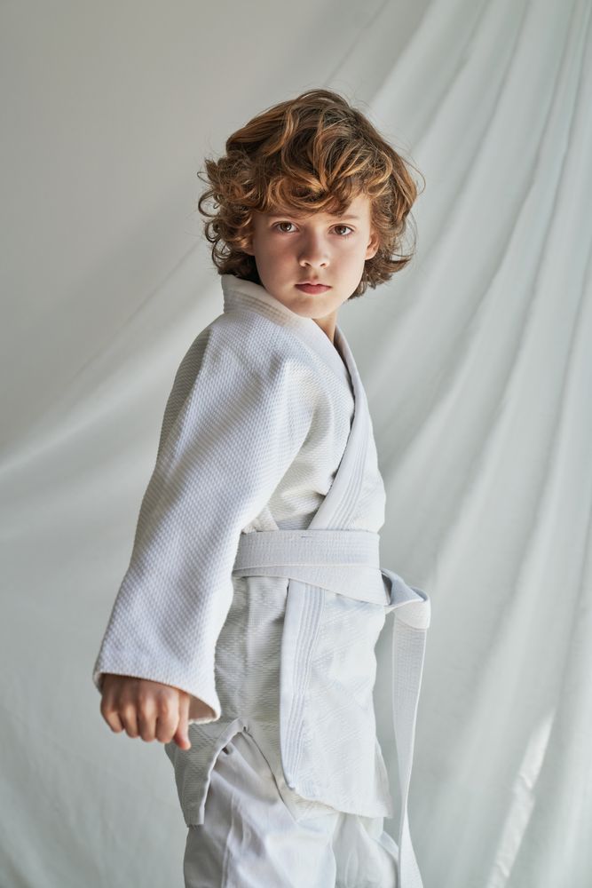 Unemotional curly haired boy in kimono near white curtain