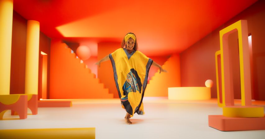Black Woman in African Outfit Dancing Energetically in Geometric Abstract Orange Environment. Creative Female Performing Modern Dance Choreography in a Studio While Looking at the Camera