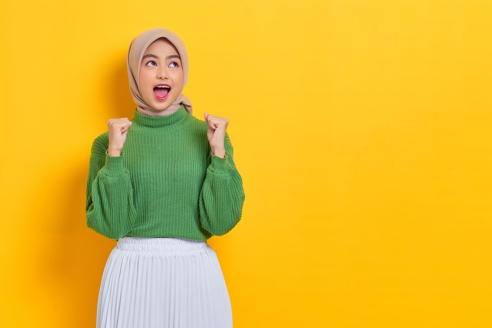 Happy woman in headscarf with both hands clenched in celebration