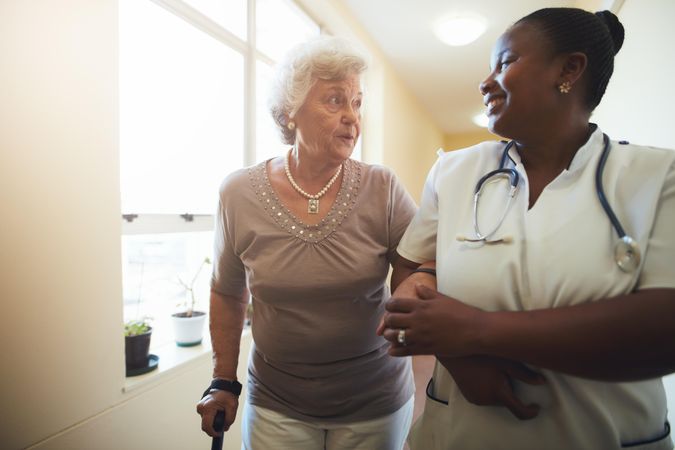 Nurse assisting mature female patient while walking in nursing home
