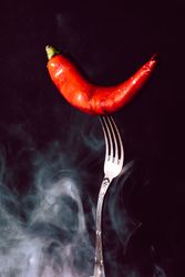 red chili pepper in fork on a dark background with smoke