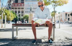Male tourist sitting outdoors on a bench and reading a city map 0yxrnb