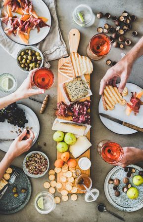 Charcuterie board with hands holding glass of rose and toasted bread