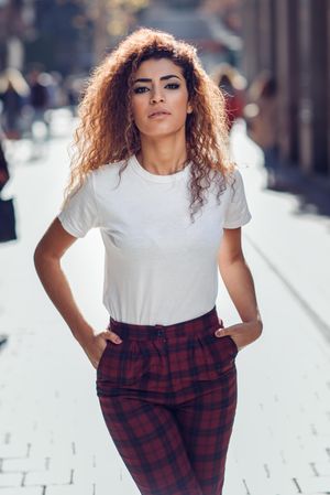 Happy Arab woman with curly hair walking down sunny street