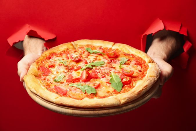 Hands hold tasty pizza on red background