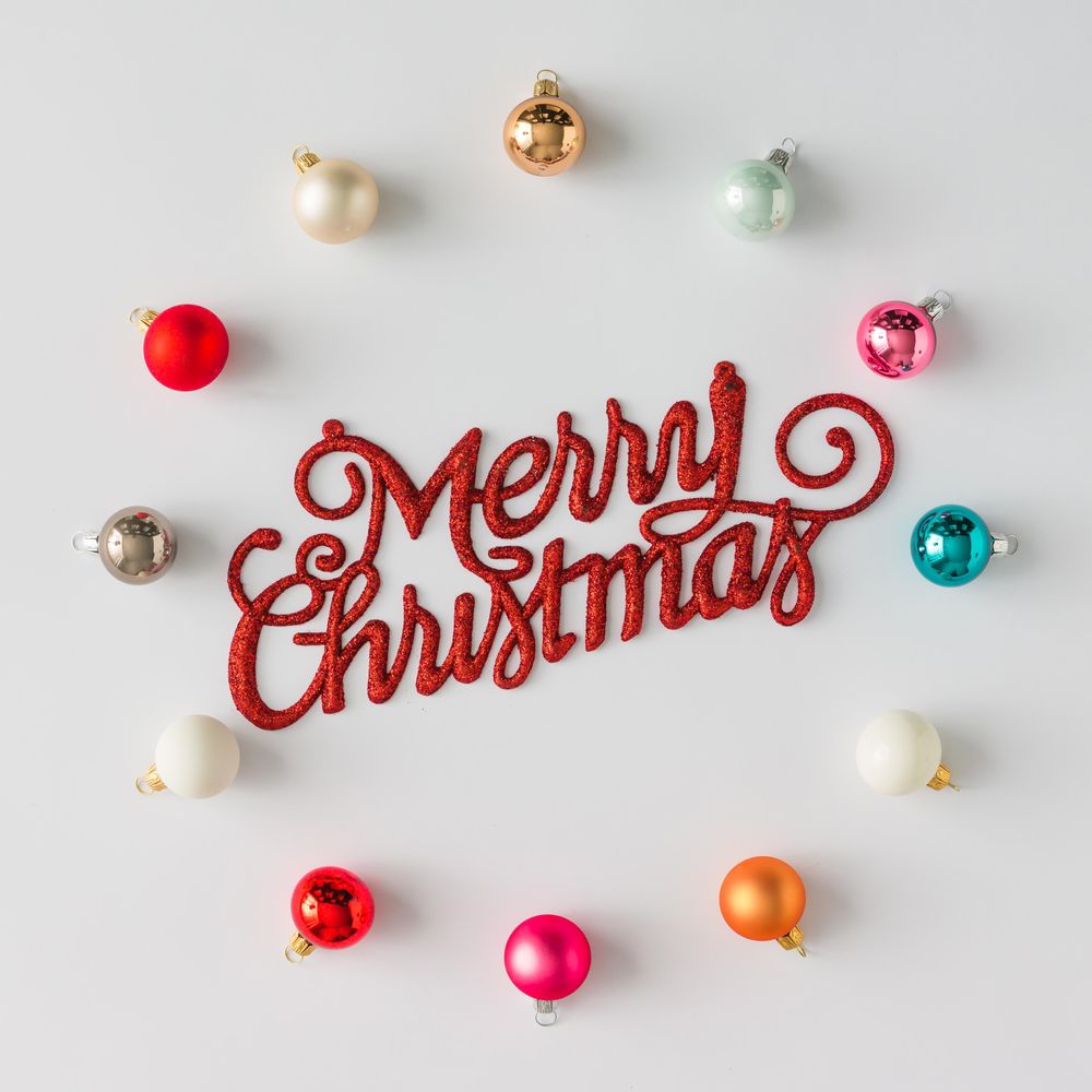 Circular border of colorful Christmas bauble decorations on light background with “Merry Christmas”