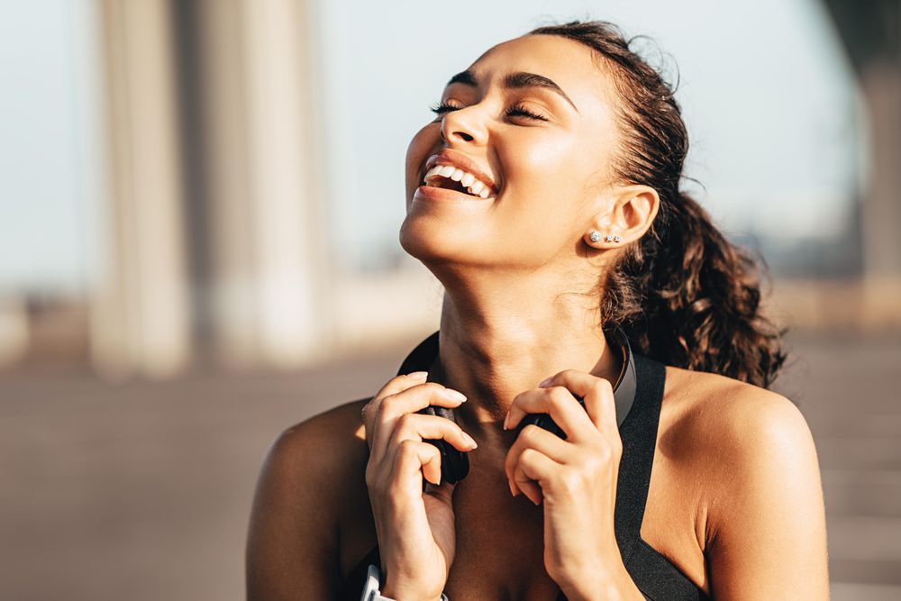 Woman holding headphones smiling with her head back