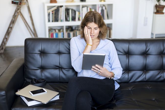 Female sitting on couch at home and shocked by something on a digital tablet