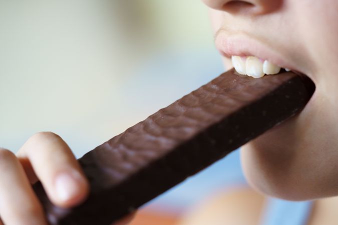 Side view of girl biting into chocolate bar