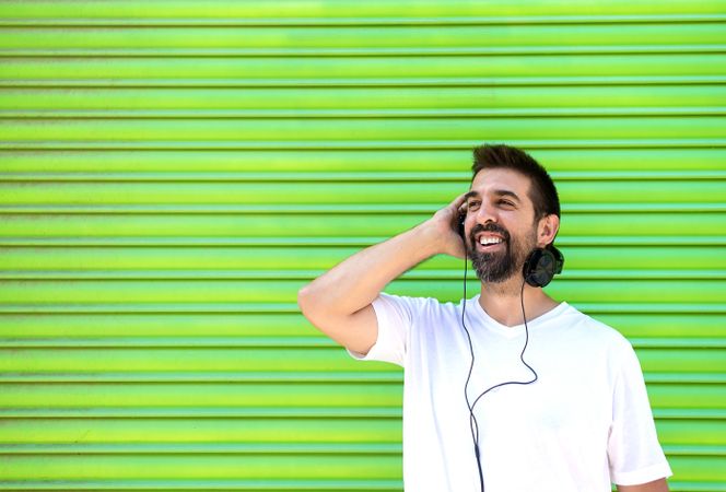 Smiling man listening to headphones in front of green background