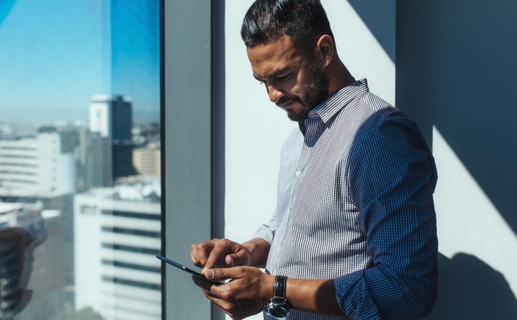 Male investor using cell phone in sunny office