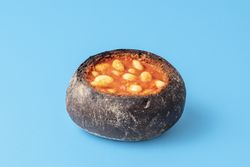 Bread bowl filled with baked beans on a blue table