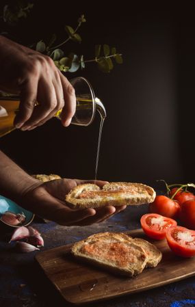 Crop person pouring oil on toasts