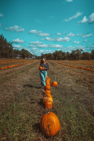 Young woman standing beside a line of pumpkins on brown field