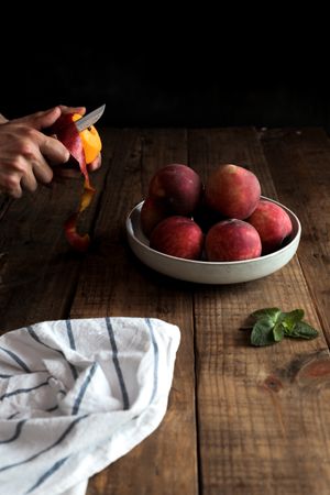 Tasty ripe peaches in plate and hands peeling peach