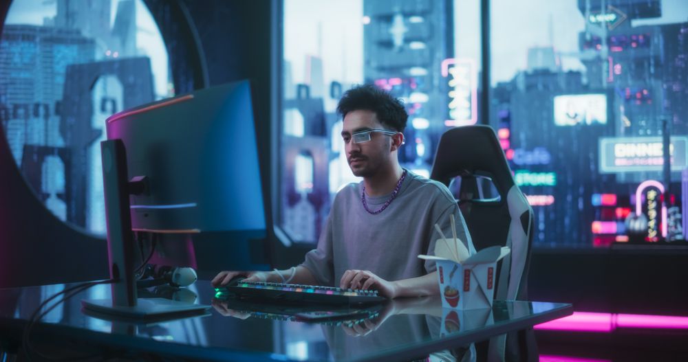 Handsome Young Man Eating Take-Away Asian Food, while Working on a Desktop Computer in a Cyberpunk Neon Room.