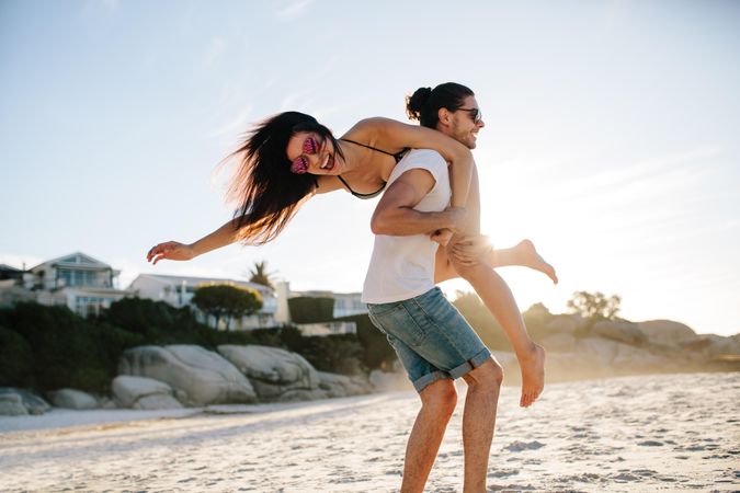 Happy young man carrying his woman on the beach