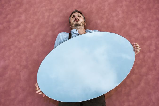 Man lying down holding mirror with reflection