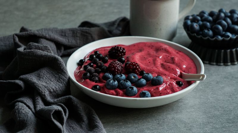 Smoothy of fresh bog blueberries and raspberries in bowl near napkin