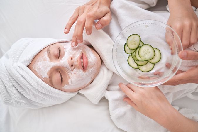 Unrecognizable woman putting cream mask with cucumber slices on