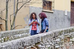 Two Black female friends smiling as their check phone while out walking