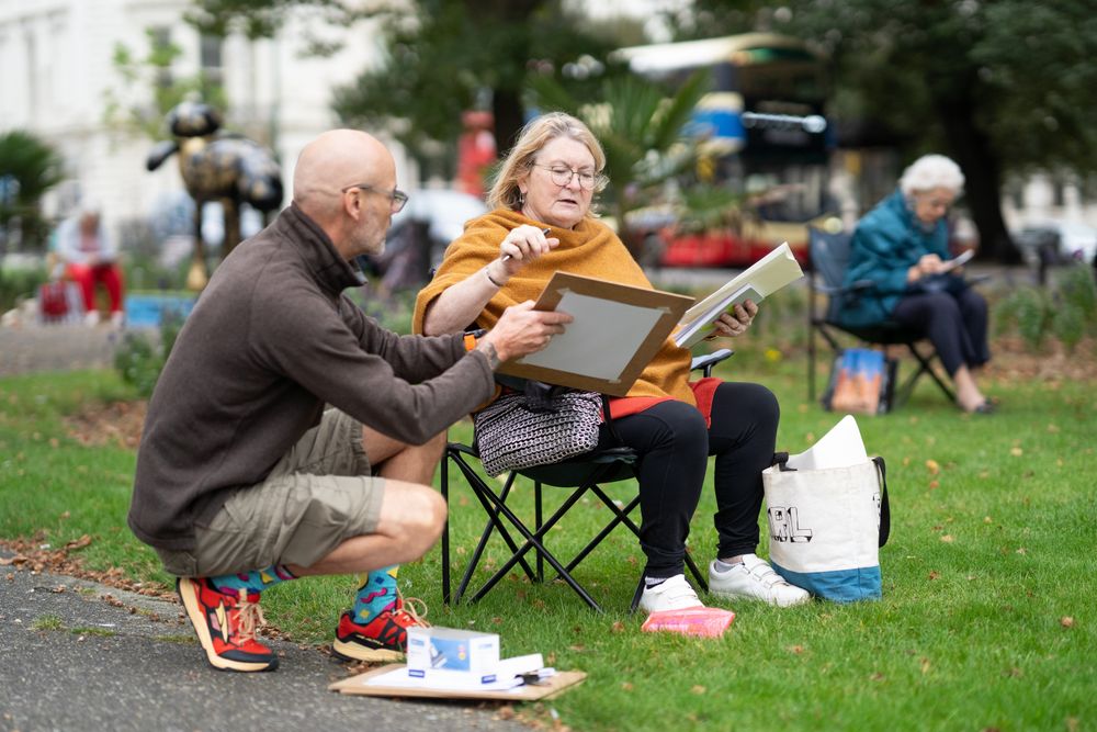 Older woman sitting calmly outside drawing talking to instructor