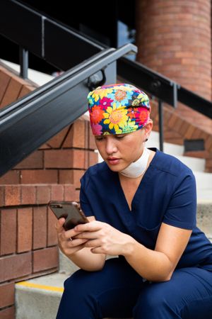 Close up of woman nurse with head covering and N95 mask around neck checking phone on break